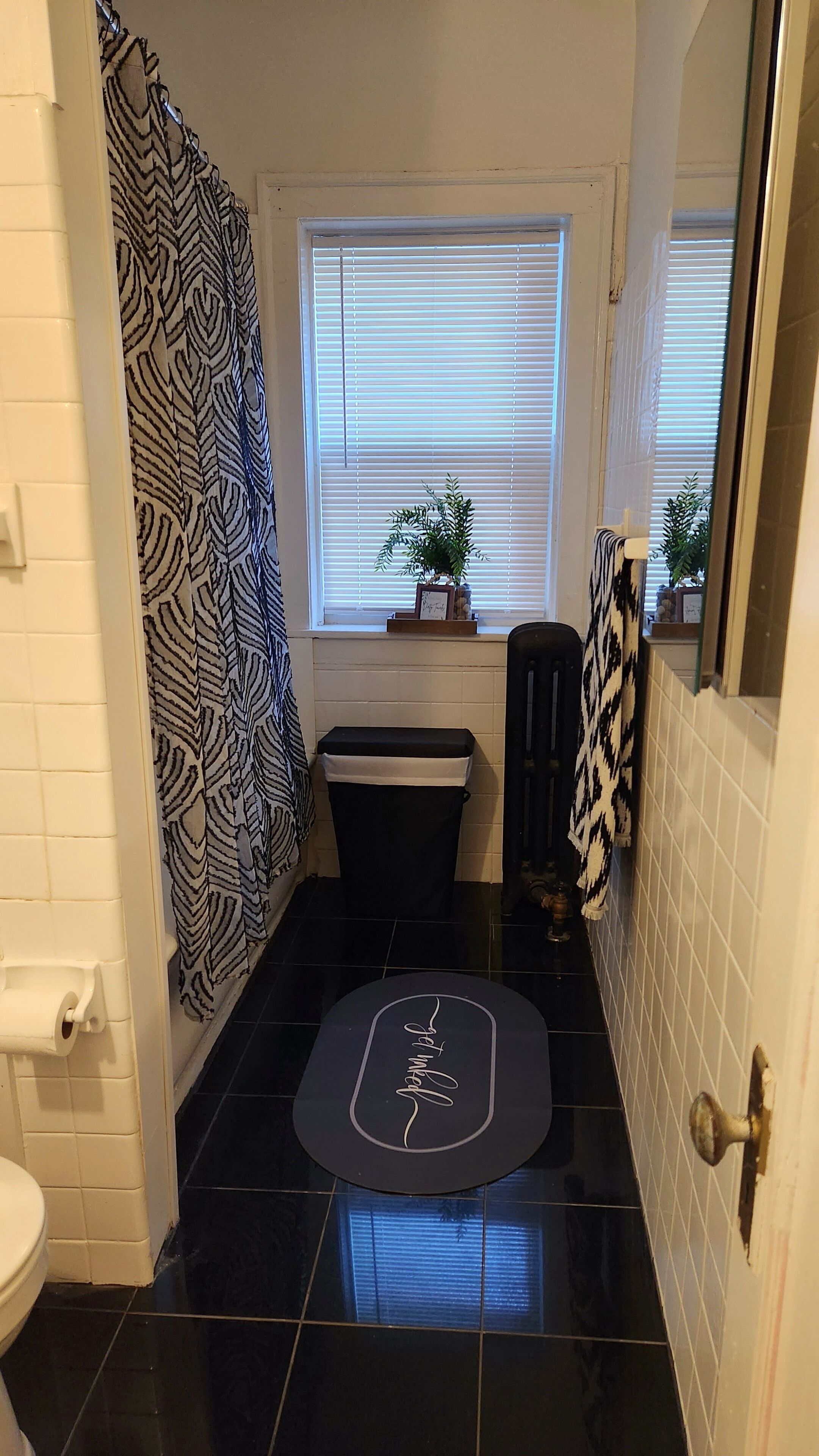 A bathroom with a black tiled floor, a toilet, a sink, a window with blinds, and a shower curtain with a leaf pattern.