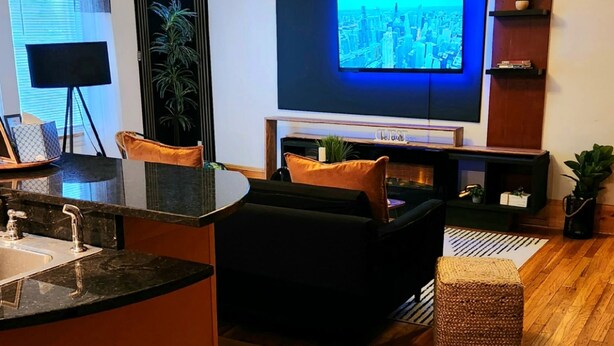 A modern living room with a flat-screen TV, a ceiling fan, and a kitchen area with a sink.