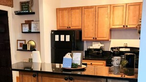 A kitchen with wooden cabinets, a black refrigerator, a microwave, and a coffee maker. There are two bar stools and a countertop with various items.