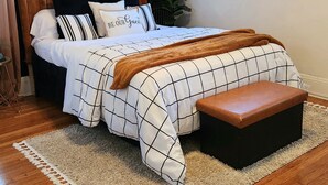 A bedroom with a bed, a bench, a plant, and a window.