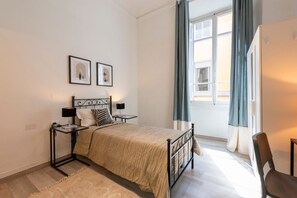 A bedroom with a bed, bedside tables, a window with curtains, and framed pictures on the wall.