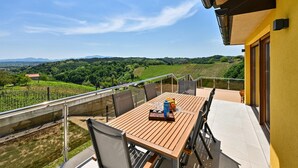 Un balcon avec une table en bois, des chaises et une vue sur les vignes et les montagnes.