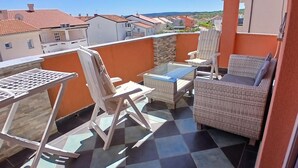 En balkon med fletmøbler, et glasbord og en metalstol.