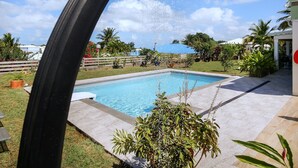 A swimming pool with a showerhead, surrounded by a garden with various plants and a clear blue sky. - Villa Oneway with swimming pool - Rated 3 stars ⭐⭐⭐ (Sainte-Rose)