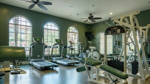 Un gimnasio con cintas de correr, elípticas, banca para press de banca y un soporte para pesas.