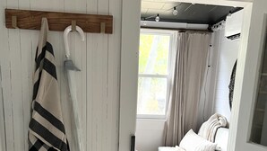 Una habitación con un sofá blanco, piso de madera, alfombra estampada y una manta a rayas colgada en la pared.