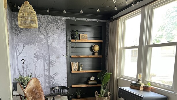 Una sala de estar acogedora con un escritorio de madera oscura, un sillón cómodo y una estantería llena de libros y objetos decorativos.