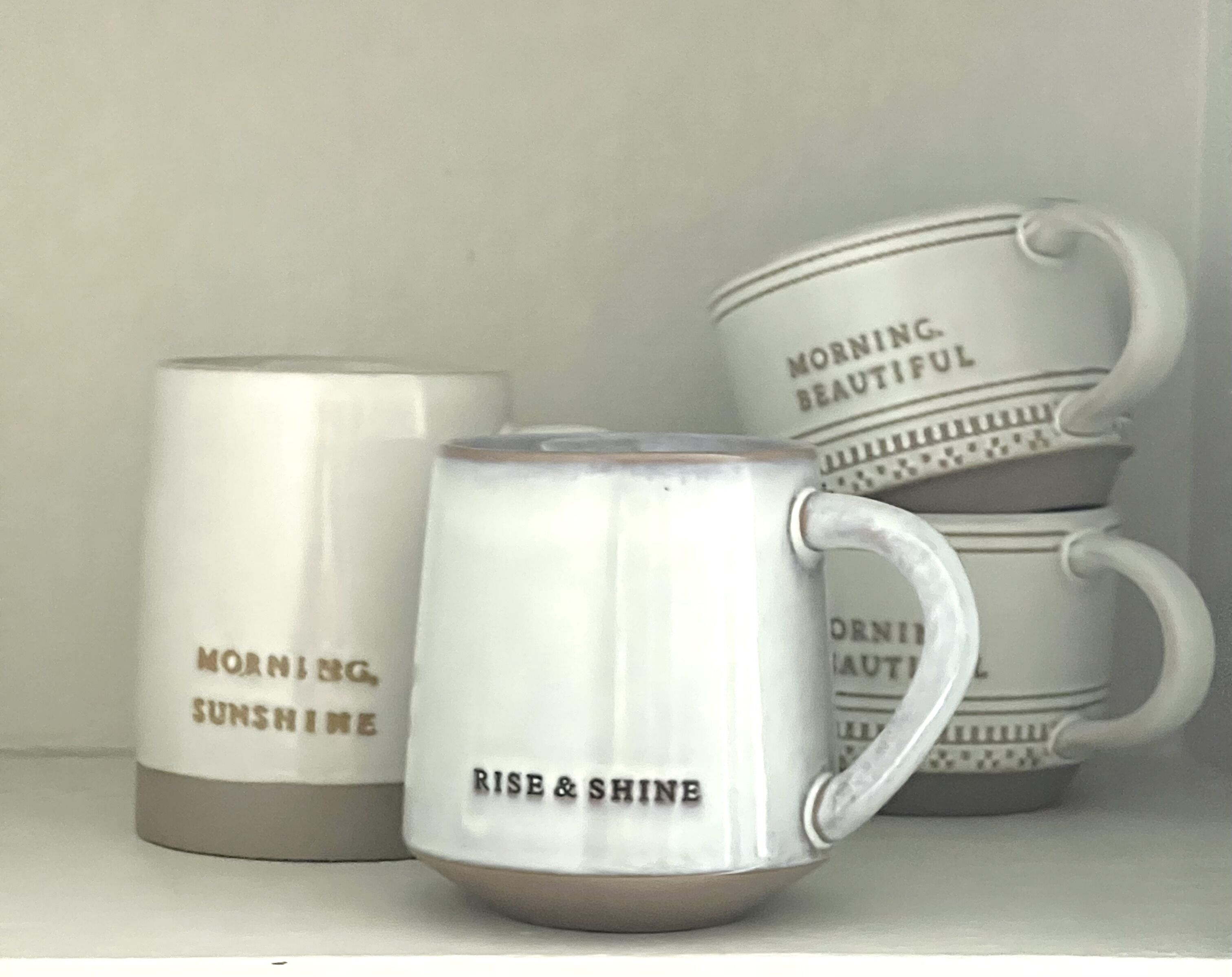 Three white ceramic mugs with handles, each featuring motivational phrases.