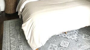 Una cama bien hecha con un cabecero oscuro, una mesita de noche con una lámpara y una planta en maceta.