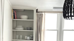 Una cocina con armarios blancos, una ventana con cortinas, un lavamanos y una mesa de comedor con un bol de fruta.