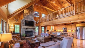A spacious living area with a stone fireplace, a high ceiling with wooden beams, a dining area with a large table, and a kitchen with modern appliances. - Good Medicine - 10 minutes to Boone! Long range views, hot tub, fire pit! (Boone)