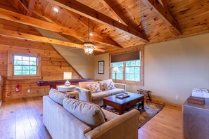 A cozy cabin interior with a wooden ceiling, a sofa, a coffee table, and a fireplace.