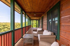 A covered porch with wicker furniture and a view of a forest.