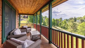A covered porch with wicker furniture and a view of a green landscape. - Good Medicine - 10 minutes to Boone! Long range views, hot tub, fire pit! (Boone)
