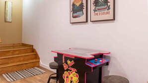 A room with a wooden staircase, a small table with arcade games, and two framed posters on the wall. - Good Medicine - 10 minutes to Boone! Long range views, hot tub, fire pit! (Boone)