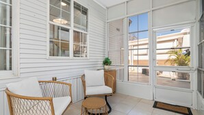 A sunlit room with white walls, a wicker chair, a cushioned chair, and a small round table.