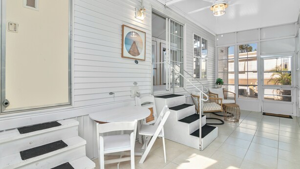 A bright, spacious room with white walls, a staircase, a dining area, and large windows offering views of the outdoors.