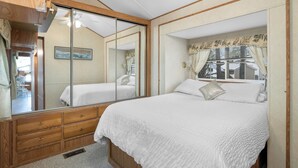 A bedroom with a large mirror, a bed with white bedding, wooden furniture, and a window with curtains.