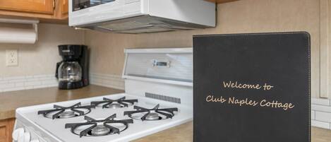 Una cocina con estufa blanca, cafetera y un cartel de bienvenida negro sobre la encimera.