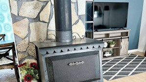 A stone fireplace with a black chimney, a television on a wooden stand, and a decorative vase with flowers. - Upper Grape, Midtown Home 2bed&1bath (Anchorage)
