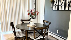 A dining area with a round table, four chairs, a woven rug, and a wall with a 'give us this day' sign. - Upper Grape, Midtown Home 2bed&1bath (Anchorage)