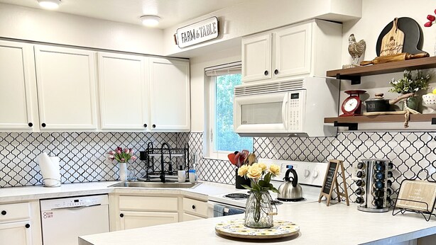 A modern kitchen with white cabinetry, a central island with stools, a microwave, and a red kettle. - Upper Grape, Midtown Home 2bed&1bath (Anchorage)