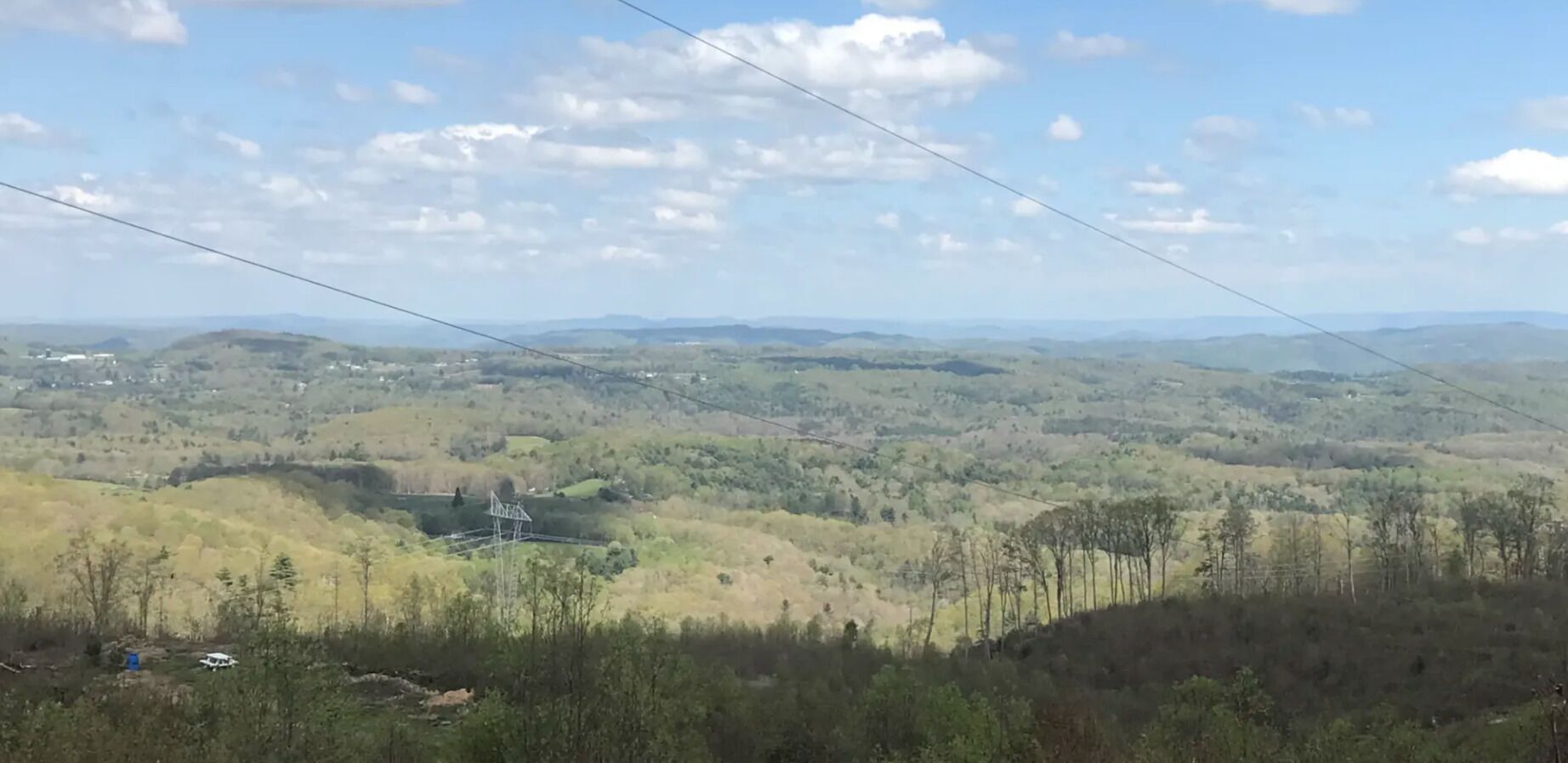 Vista panorámica de un paisaje montañoso con una línea eléctrica, un edificio pequeño y vegetación escasa.