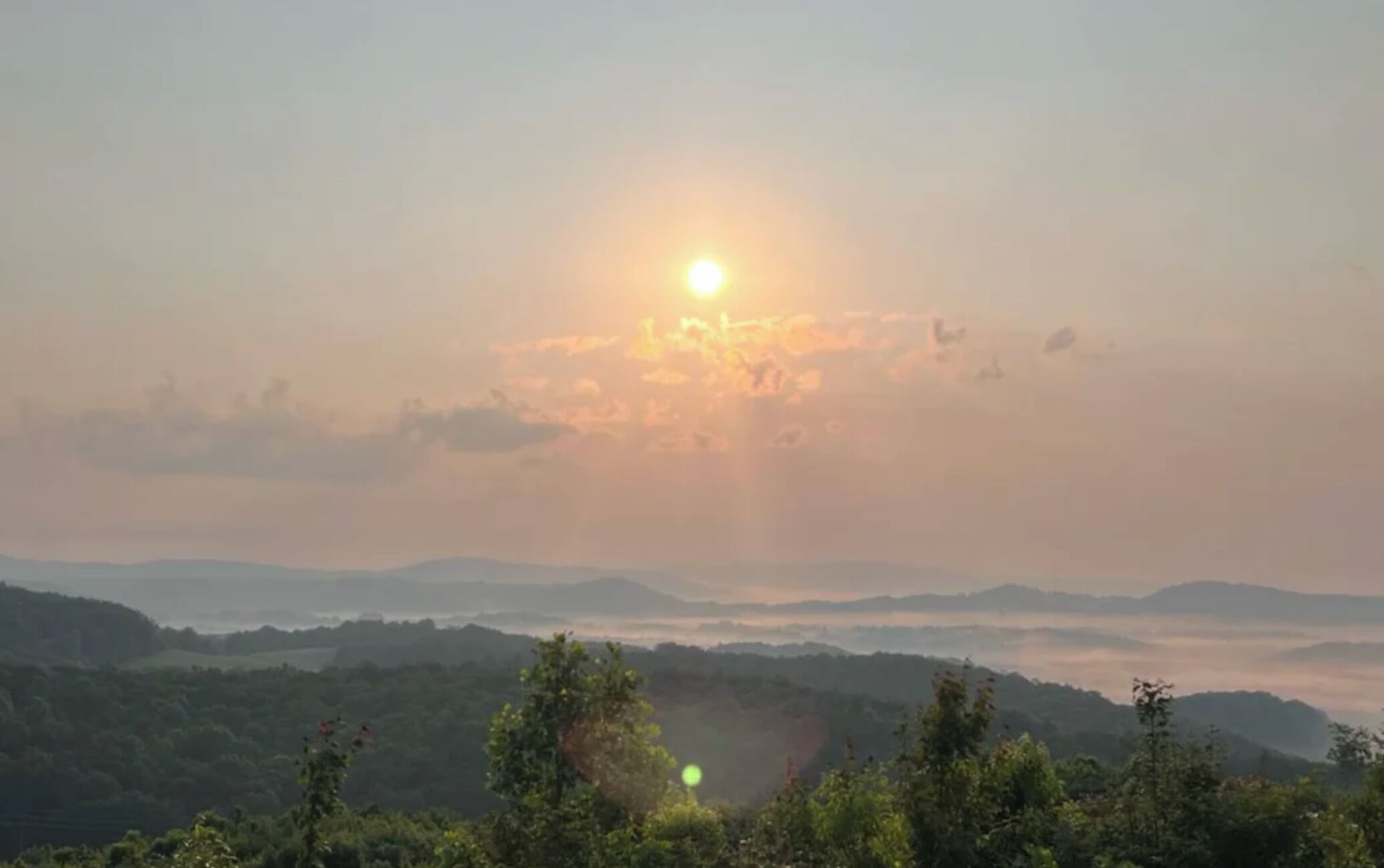 A landscape with a sun setting behind a range of hills.