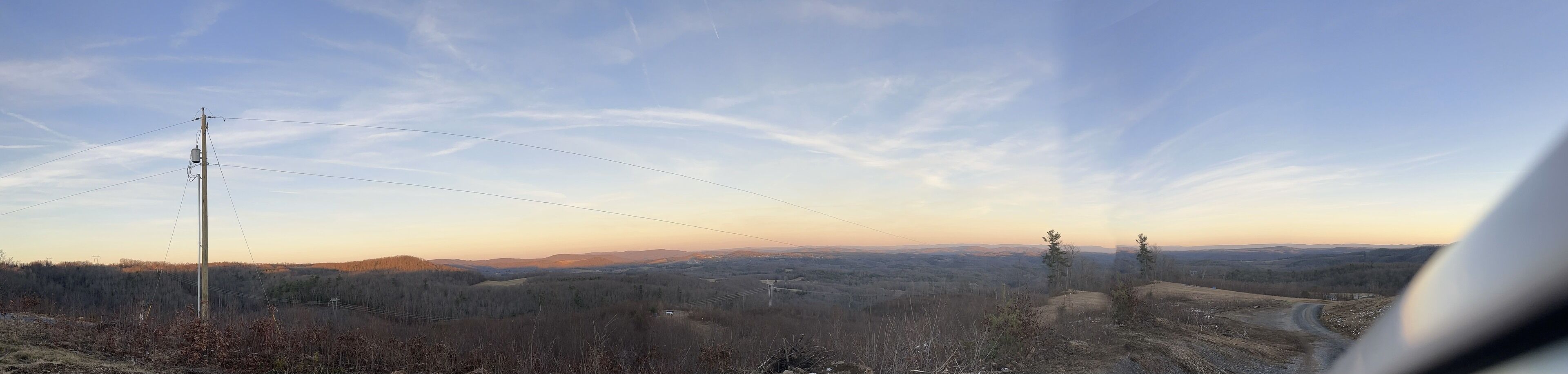 Ein weiter Panoramablick auf eine hügelige Landschaft mit blauem Himmel, Stromleitungen und einer unbefestigten Straße.