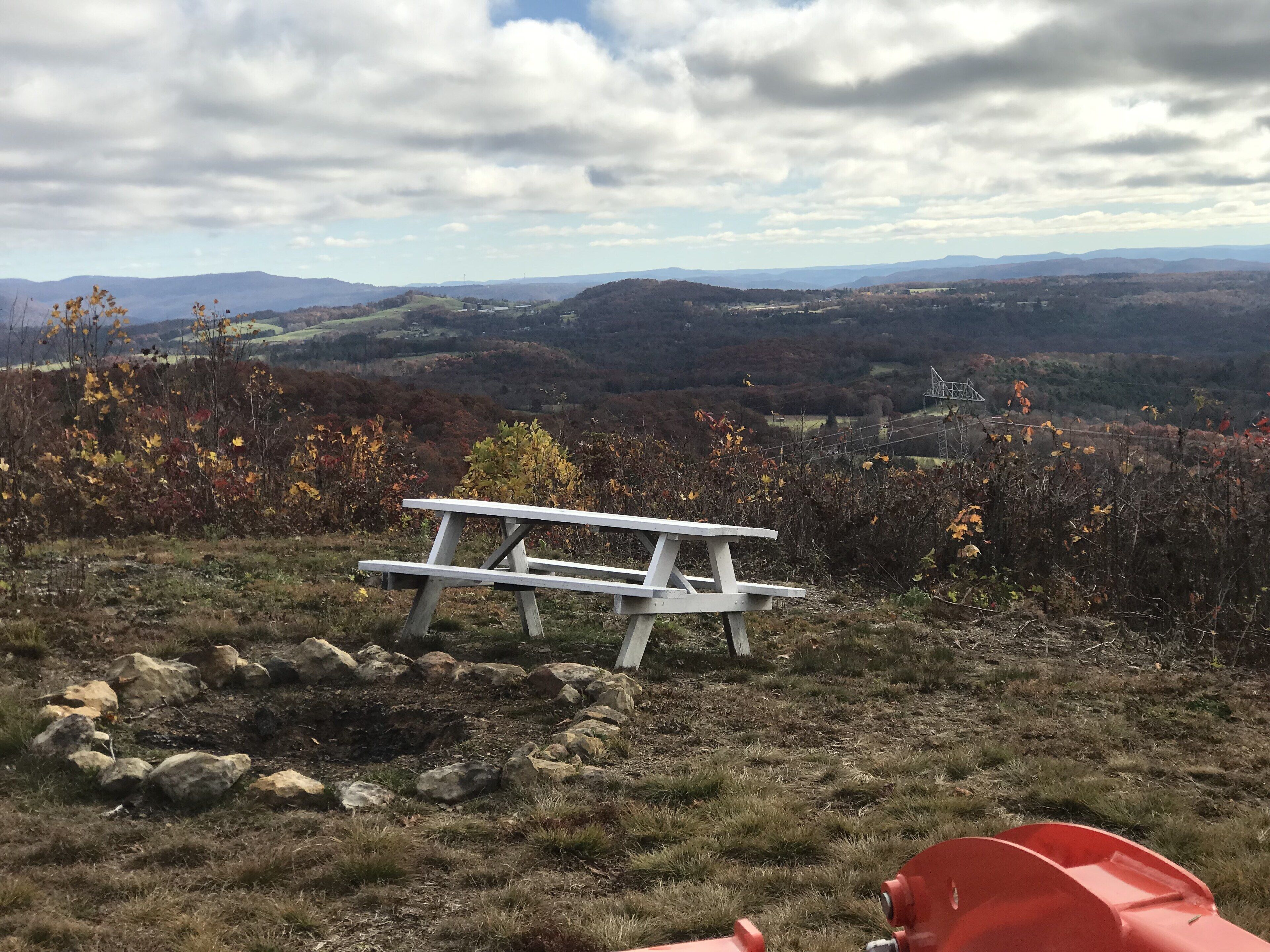 Une table de pique-nique sur une colline herbeuse, offrant une vue sur les montagnes lointaines et le feuillage automnal.