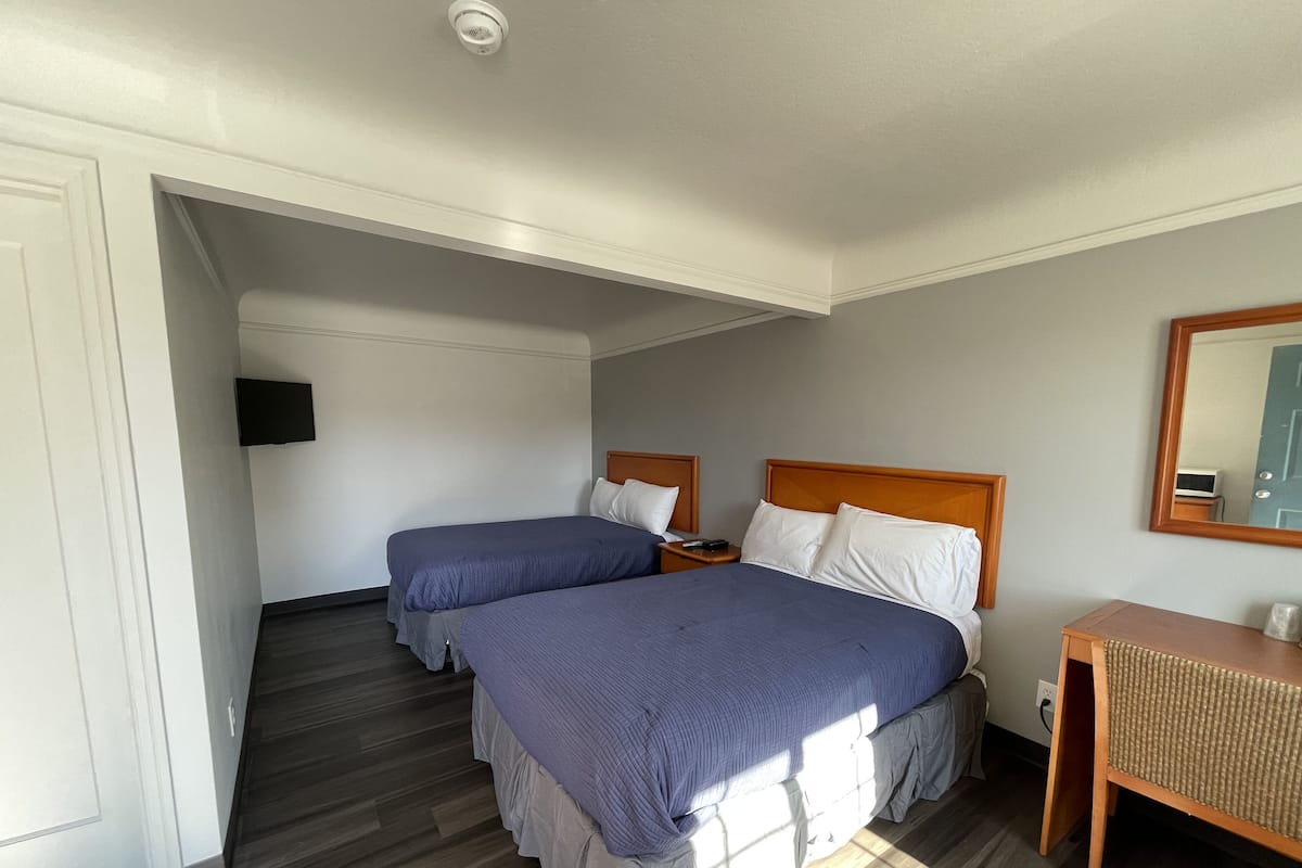 A hotel room with two beds, a TV, a bedside table, and a mirror.