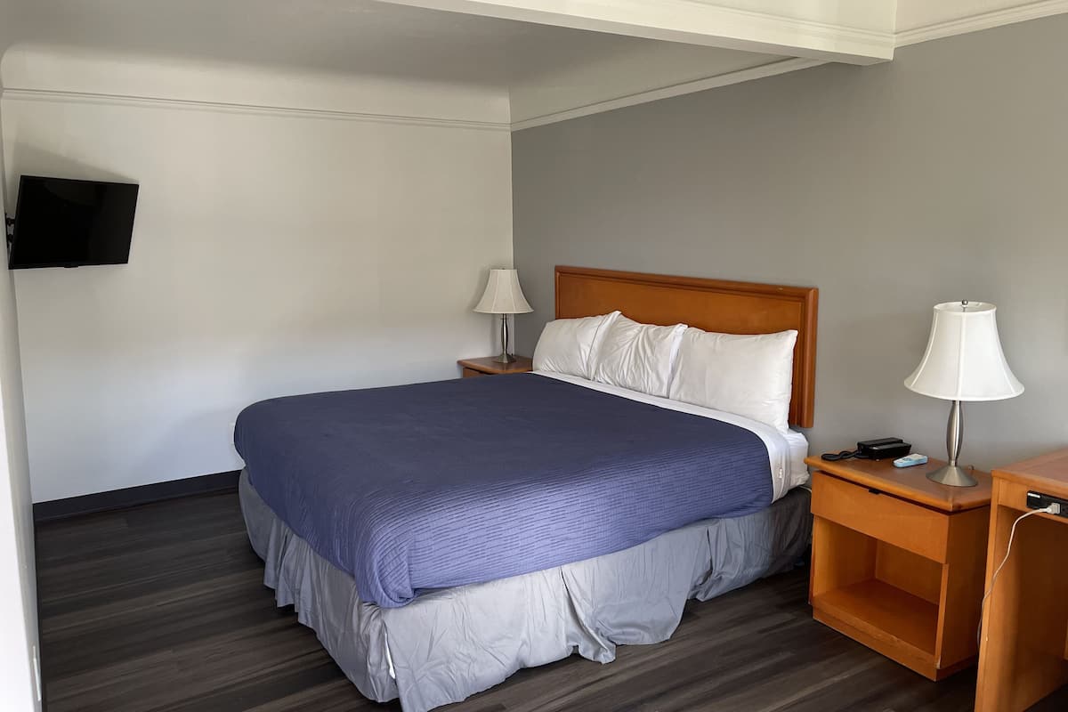 A hotel room with a bed, two bedside tables, a TV mounted on the wall, and a wooden nightstand.
