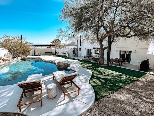Patio trasero con piscina, sillas de descanso y una parrilla.