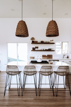 Una cocina moderna con una isla central, cuatro sillas de mimbre y lámparas colgantes.