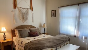 Une chambre bien rangée, avec un lit, des lampes de chevet, un banc et une fenêtre équipée de stores.