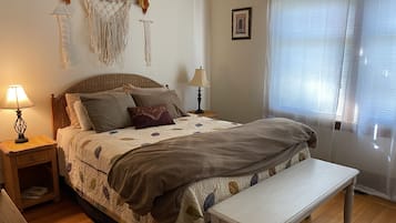 A neatly arranged bedroom with a bed, bedside lamps, a bench, and a window with blinds.