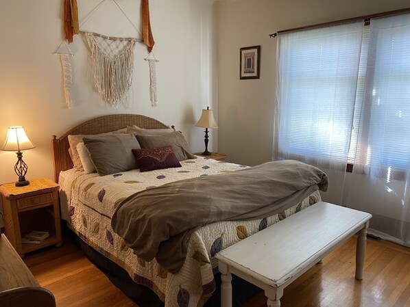 A neatly arranged bedroom with a bed, bedside lamps, a bench, and a window with blinds.