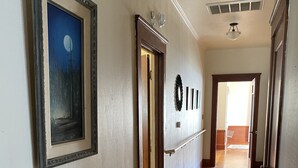 Un couloir au sol en bois, un tableau encadré accroché au mur et une porte donnant sur une autre pièce.