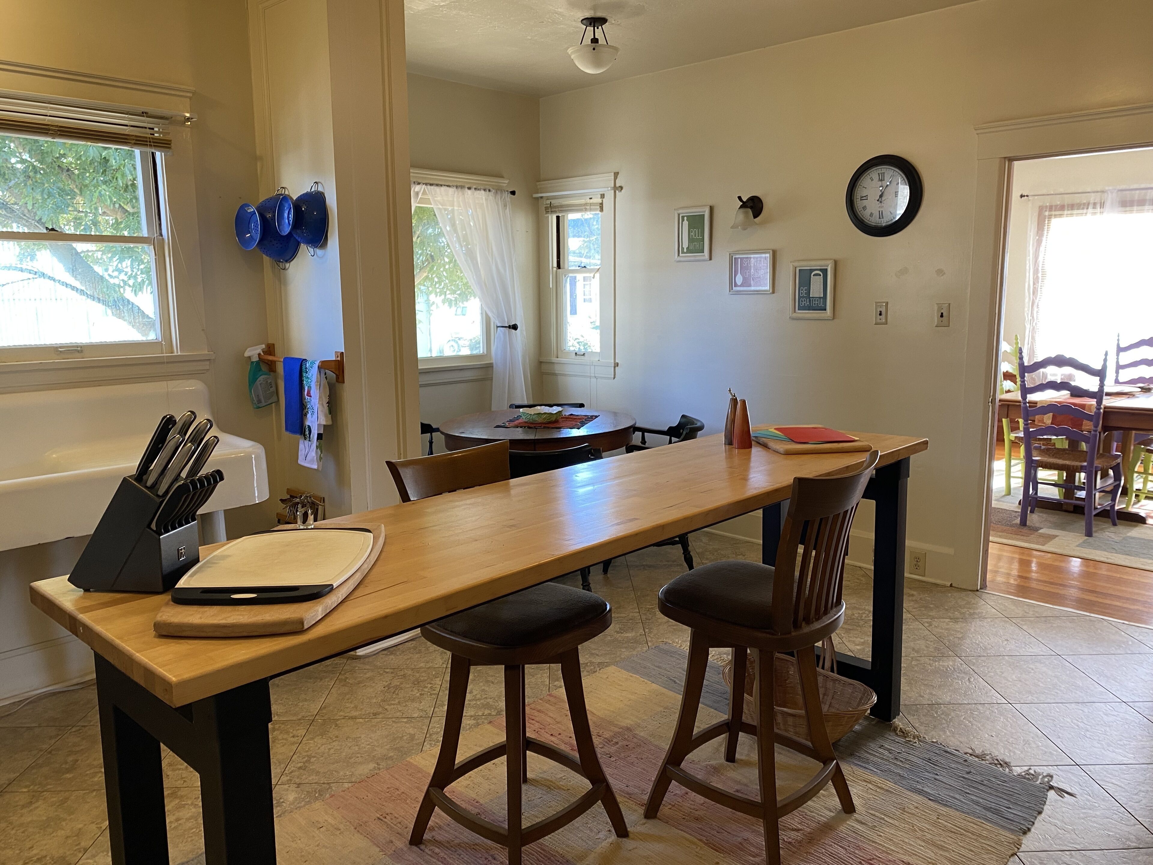 Una cocina con una mesa de madera, taburetes de bar y una ventana con persianas.