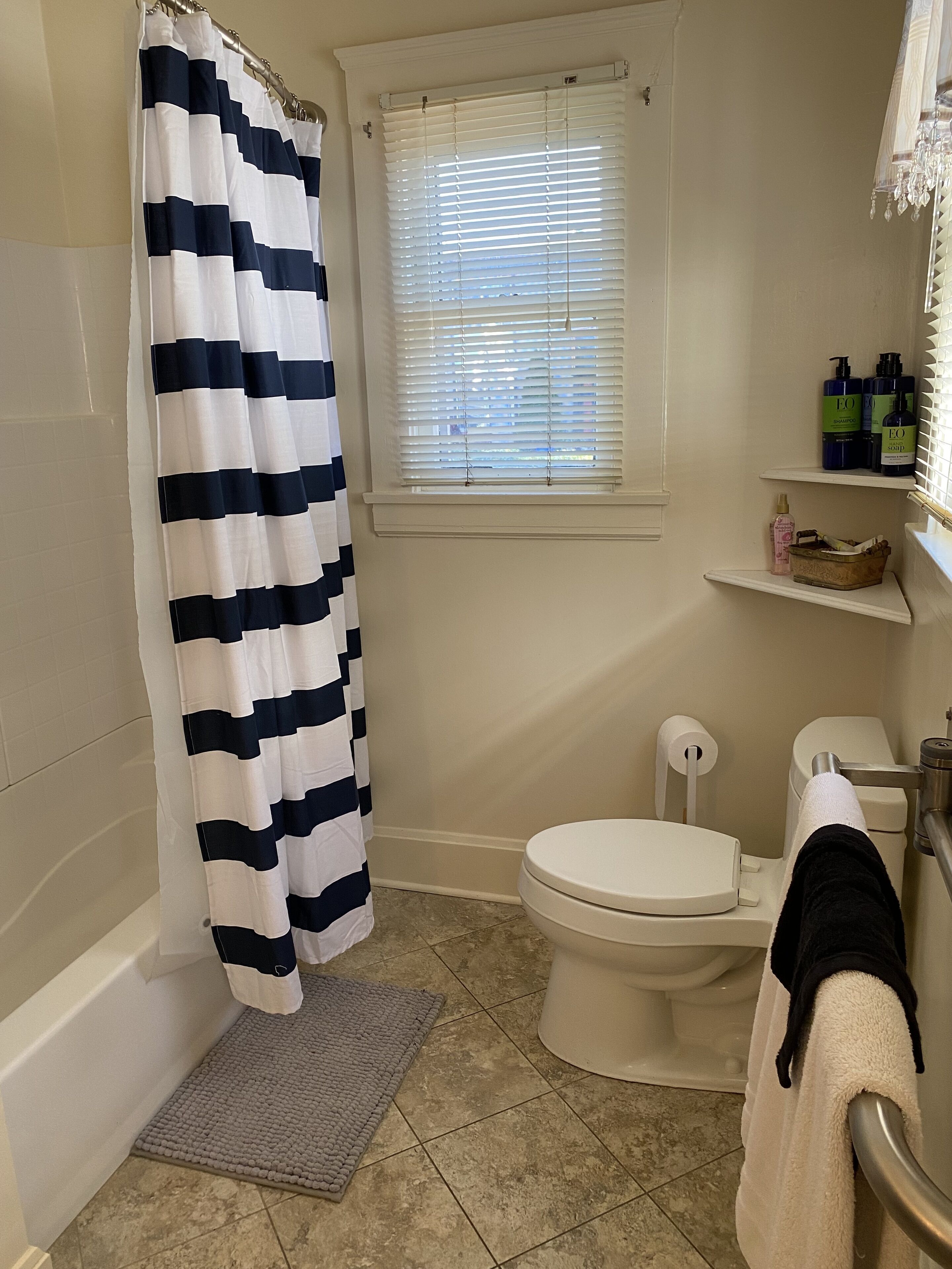 Un baño con bañera, inodoro y ventana con persianas.