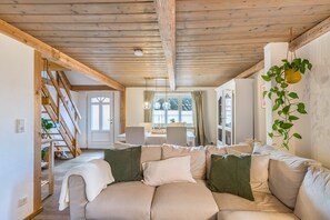 Ein gemütliches Wohnzimmer mit Holzboden, einer Couch mit Kissen, einem Essbereich mit Tisch und Stühlen sowie einer Treppe.