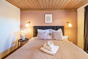 Ein Schlafzimmer mit Holzboden, einem Bett mit Kopfteil, zwei Nachttischlampen, einem gerahmten Kunstwerk und einem kleinen Tisch mit einer Vase.
