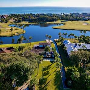 Un parcours de golf avec un étang, des palmiers et un bâtiment doté d’un toit bleu.