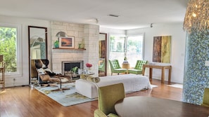 Un salon moderne avec une cheminée, des fauteuils verts, une table à manger et une vue sur la verdure à l’extérieur.