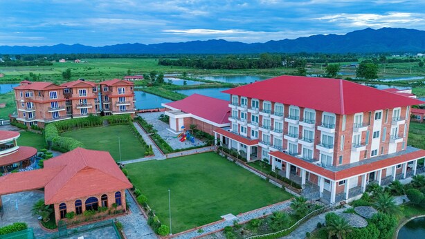 A hotel with multiple buildings, a playground, and a large green lawn. - Lumbini Green Resort (Shivaraj)