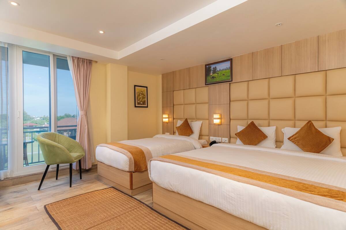 Une chambre d’hôtel avec deux lits, une grande fenêtre donnant sur un beau paysage, un fauteuil vert et un téléviseur fixé au mur.