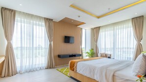 A modern hotel room with a large bed, a flat-screen TV mounted on the wall, and a view of the city through large windows. - Lumbini Green Resort (Shivaraj)
