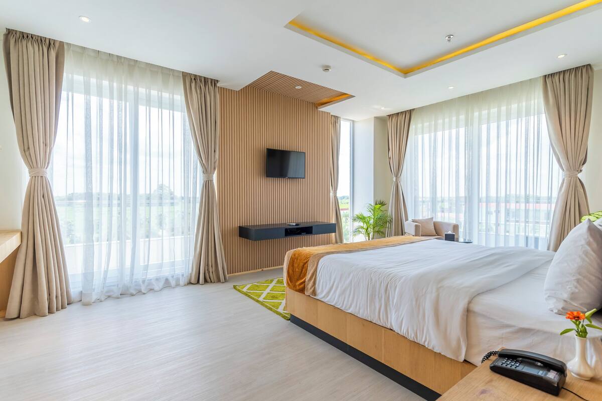 Une chambre d’hôtel moderne dotée d’un grand lit, d’un téléviseur à écran plat fixé au mur et offrant une vue sur la ville grâce à de grandes fenêtres.