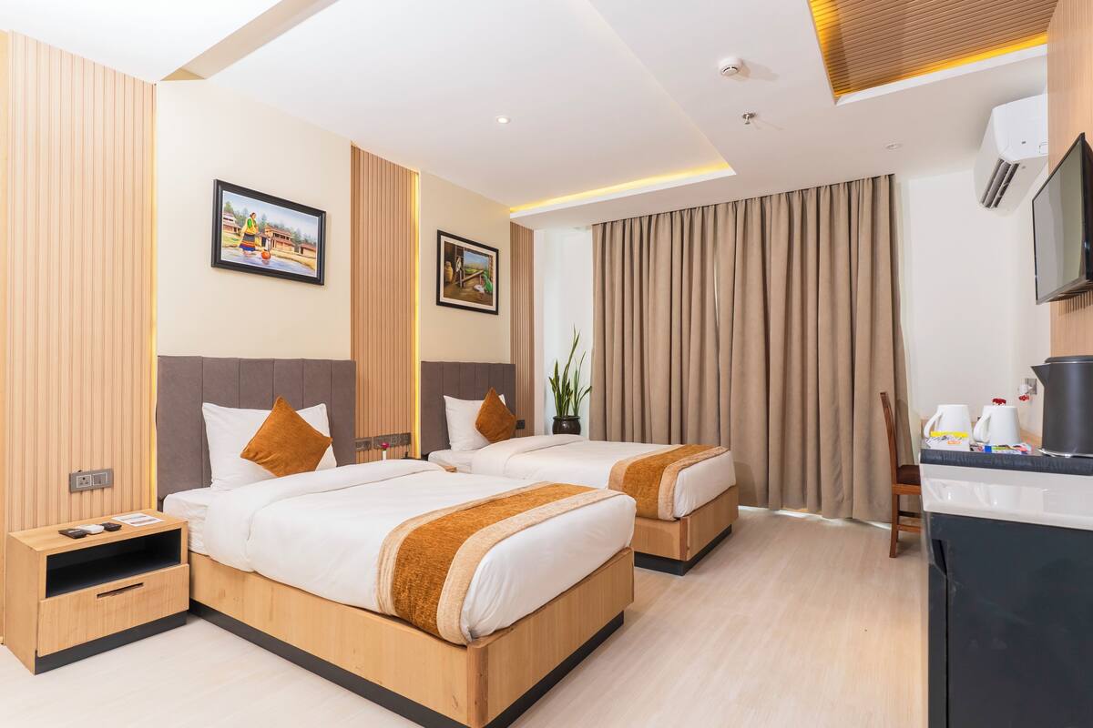 Une chambre d’hôtel avec deux lits, un bureau, une télévision et une fenêtre avec des rideaux.