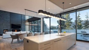 A modern kitchen with a large island, a fireplace, and a view of the outdoors.